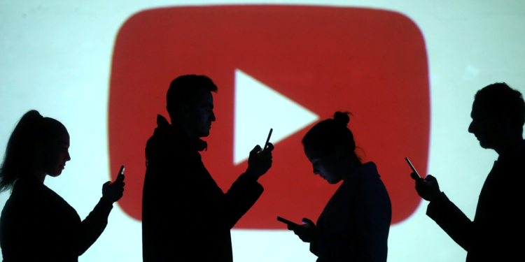 Silhouettes of mobile users are seen next to a screen projection of Youtube logo in this picture illustration taken March 28, 2018.  REUTERS/Dado Ruvic/Illustration - RC1D24345500