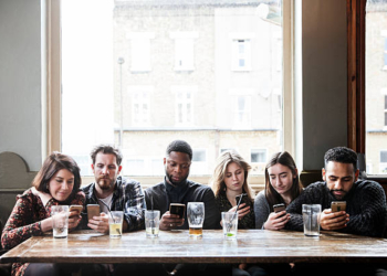 6 friends at a pub with phones, all online, concentrated, having a good time,