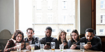 6 friends at a pub with phones, all online, concentrated, having a good time,