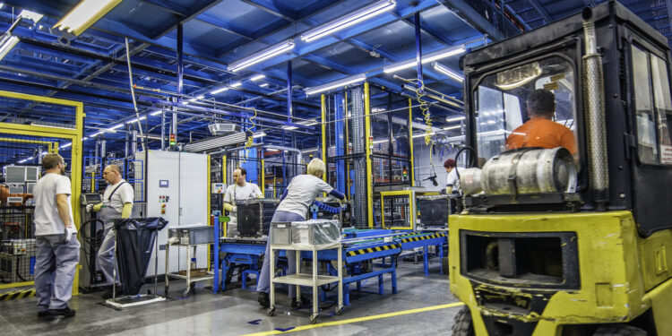 Factory workers doing their jobs while a forklift is driving by.
